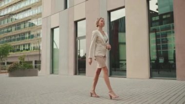 Businesswoman in beige suit walks outside past business building