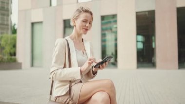 Businesswoman with blond hair using cellphone outside on the street