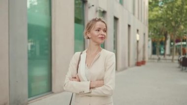 Smiling woman with blond hair wearing beige suit walks down the street and looks around