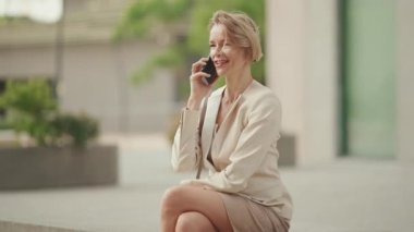 Businesswoman with blond hair talking on cellphone, looking at wrist watch