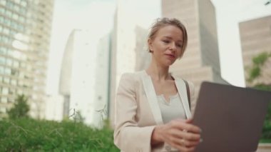 Businesswoman with blond hair wearing beige suit is using pc laptop outside