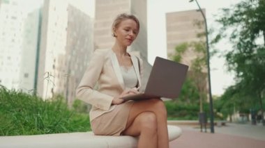 Businesswoman with blond hair wearing beige suit is using pc laptop outside