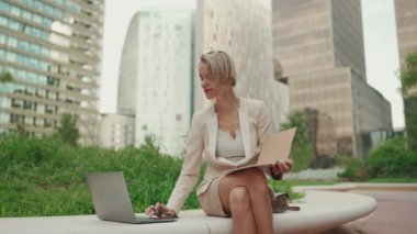 Businesswoman with blond hair wearing beige suit uses pc laptop, writes notes