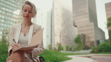 Businesswoman with blond hair wearing beige suit writes notes