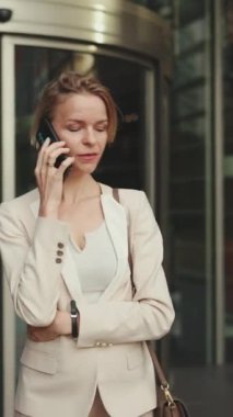 VERTICAL VIDEO: Businesswoman leaves the business center, talking on the cellphone