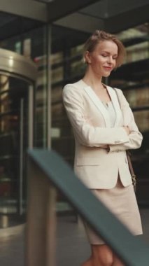 VERTICAL VIDEO: Businesswoman with blond hair wearing beige suit leaving business center
