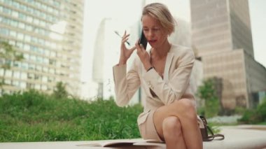 Businesswoman with blond hair wearing beige suit talking on cellphone, looking through notes