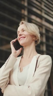 VERTICAL VIDEO: Happy businesswoman with blond hair talking on cellphone, good deal, success
