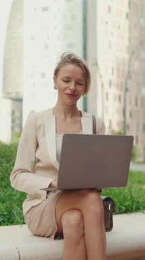 VERTICAL VIDEO: Businesswoman with blond hair wearing beige suit is using pc laptop outside