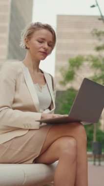 VERTICAL VIDEO: Businesswoman with blond hair wearing beige suit is using pc laptop outside