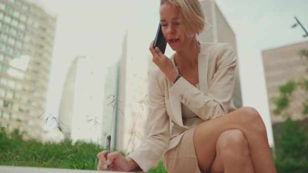 Businesswoman Blond Hair Wearing Beige Suit Talking Cellphone Writes Notes — Videoclip de stoc