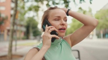 Close up, beautiful happy smiling woman with short blond hair in casual wear sits on bench, talking on cellphone