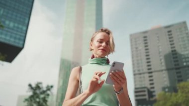 Friendly woman with short blonde hair in casual clothes looking at map trying to find his way using his mobile phone. Woman using map app in cellphone outdoors