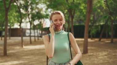 Beautiful smiling woman with short blond hair in casual clothes walks through the city square, talking on cellphone