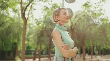 Beautiful smiling woman with short blond hair in casual clothes walks through the city square. Backlight