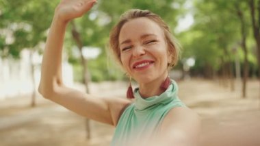 Beautiful happy woman with short blond hair in casual wear using cellphone, making video call