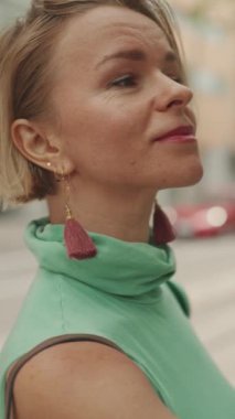 VERTICAL VIDEO: Close up, beautiful woman with short blond hair in casual clothes stands at tram stop, looks at the public transport timetable on the information board