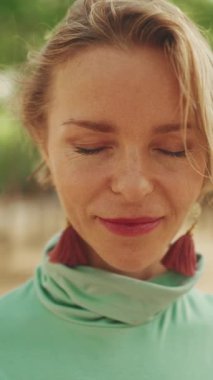 VERTICAL VIDEO: Close-up of an attractive happy woman with short blond hair wearing casual clothes, opens her eyes, smiles looking at the camera