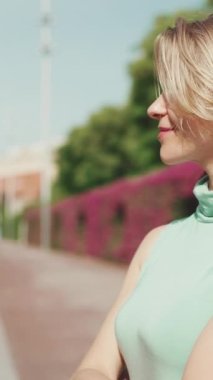 VERTICAL VIDEO: Attractive happy woman with short blond hair wearing casual clothes crosses the road at crosswalk
