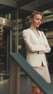 VERTICAL VIDEO: Businesswoman with blond hair wearing beige suit leaving business center