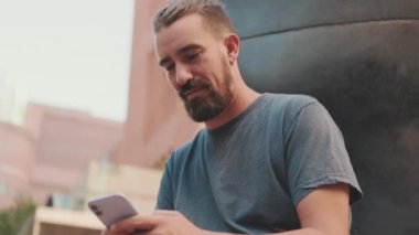 Young adult man with beard uses phone outside