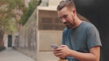 Young adult smiling man with beard uses phone from outside