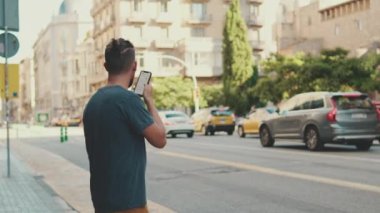 Young man with beard uses cellphone while standing on crosswalk, sends voice message