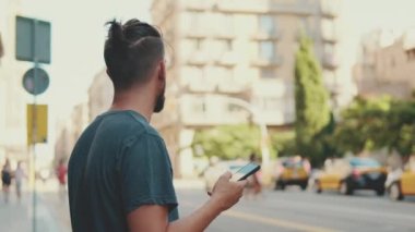 Young man with beard uses cellphone while standing on crosswalk