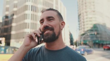 Close-up of young man with beard talking on the phone on traffic cars background