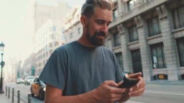 Young man with beard walks down the street using cellphone