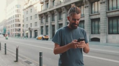 Young smiling man with beard stands on street using cellphone