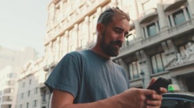 Young man with beard walks down the street using cellphone