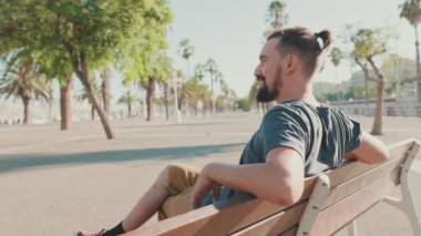 Young smiling man with beard sits and rests on bench
