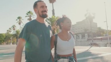 Happy interracial couple walking talking and smiling down the street holding hands