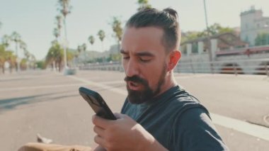 Close up, young man with beard sits on bench emotionally talking on cellphone