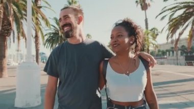 Happy interracial couple walking down the street talking and smiling. Man hugs the woman. Backlight