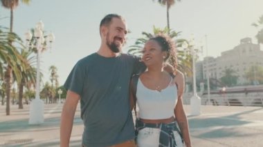Happy interracial couple walking down the street talking and smiling. Man hugs the woman