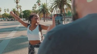 Smiling interracial couple. Man takes picture and video of woman on the phone