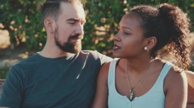 Close up, interracial couple talking while sitting on bench