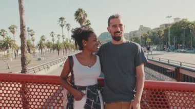 Happy interracial couple talking while standing on the bridge, hugging, kissing