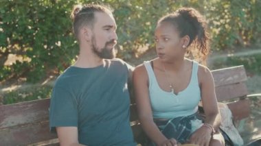 Interracial couple talking while sitting on bench. Backlight
