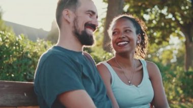 Happy smiling interracial couple talking while sitting on bench. Backlight
