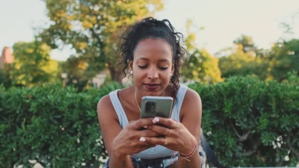 Smiling Young Mixed Race Woman Sitting Park Bench Using Cellphone — Αρχείο Βίντεο