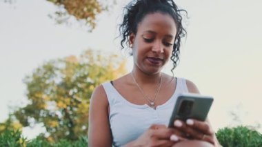 Young mixed race woman sits on park bench, uses cellphone