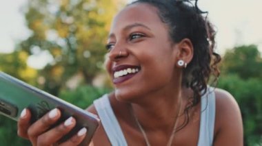 Close-up of laughing young mixed race woman sitting on park bench talking on speakerphone