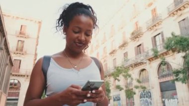 Young mixed race woman walks along the street of the old city, uses cell phone
