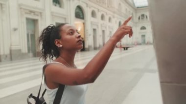 Young mixed race woman stands at the railway station, looks at the information board