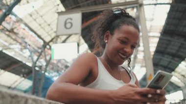 Close up, young mixed race woman sitting at the railway station, using cellphone