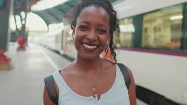 Close-up of smiling young mixed race woman standing at railway station on trains background