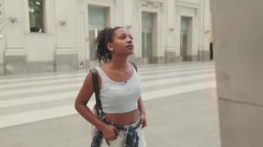 Young mixed race woman stands at the railway station, looks at the information board